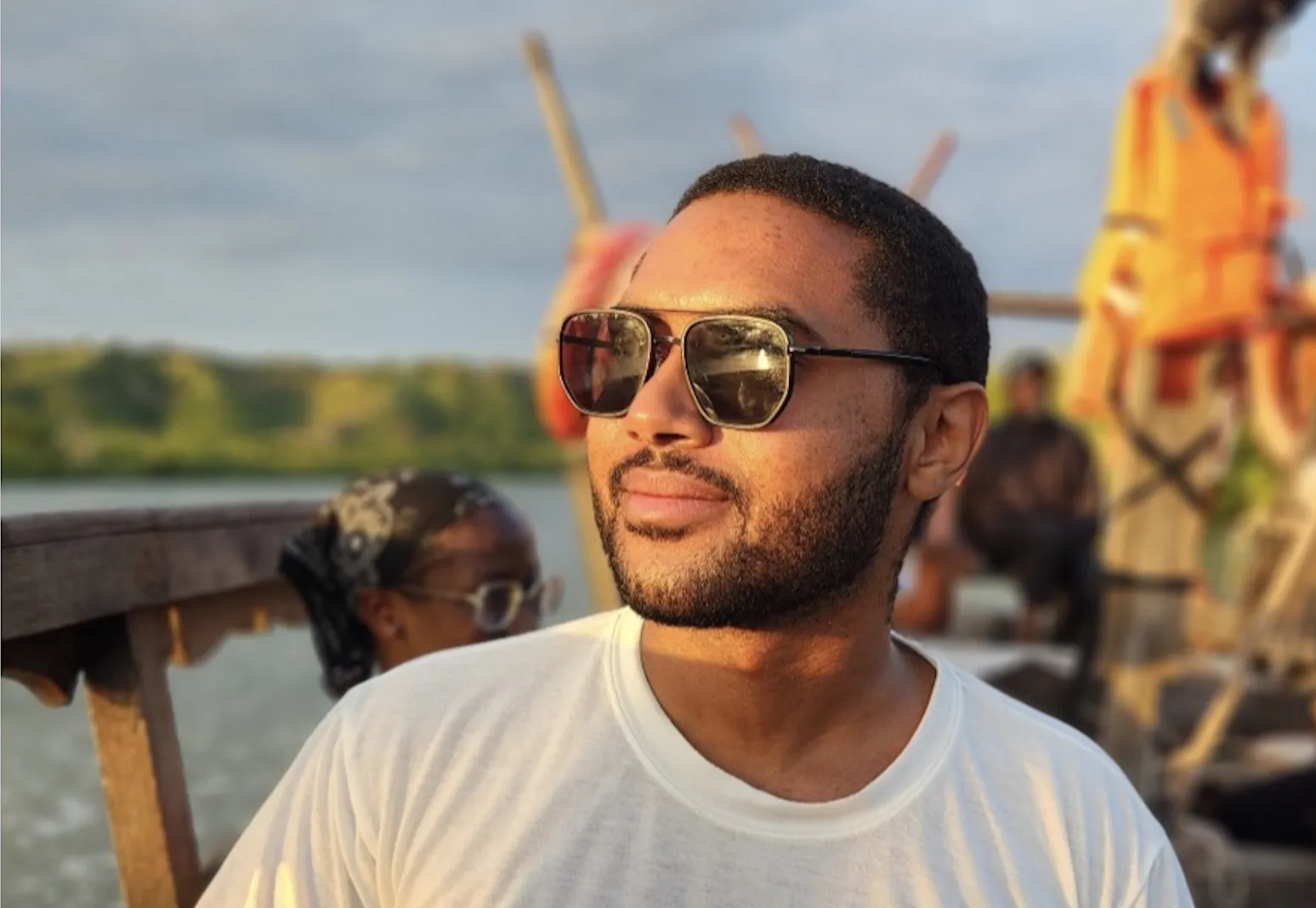 Kiwi Kiwinda wearing sunglasses and sitting by water.