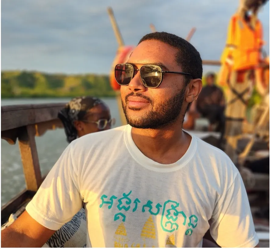 Kiwi Kiwinda wearing sunglasses sitting by the water.